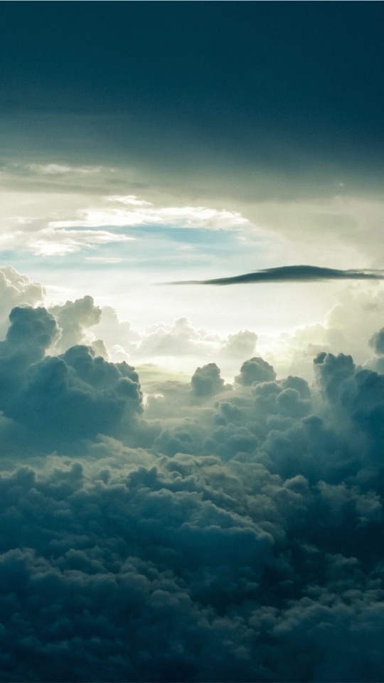 青緑がかった色調で、雲海と雲間から差す光を上空からとらえた幻想的な風景写真。