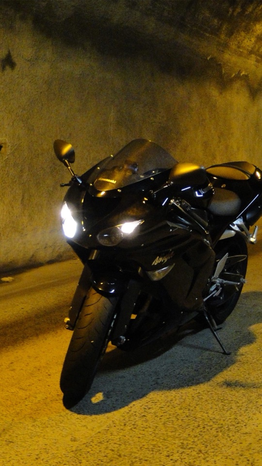 暗いトンネルの中で、ヘッドライトを灯した黒いスポーツバイクを正面からとらえた写真。
