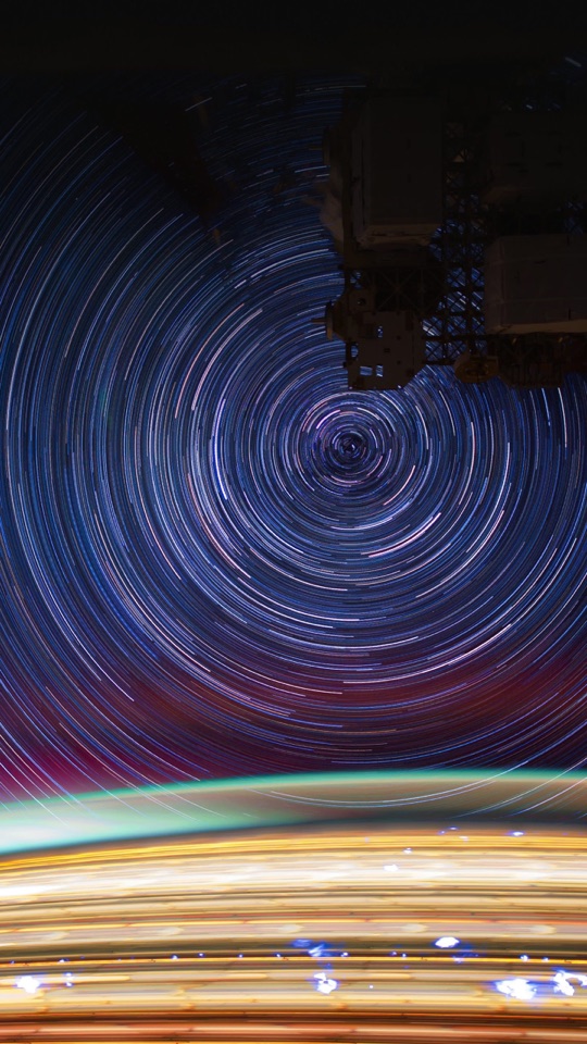 暗い夜空に、天の極を中心に星が渦を巻くように軌跡を描く長時間露光の写真。