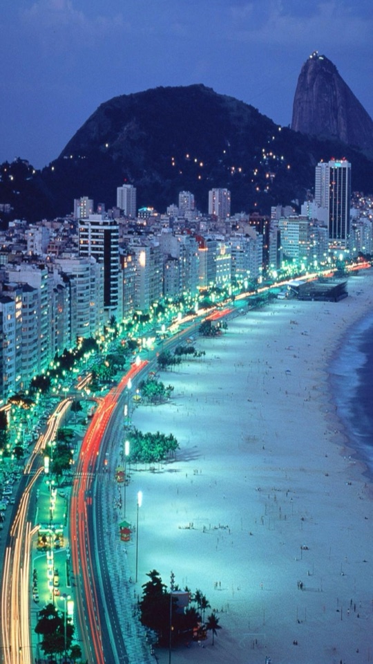夜、湾曲した海岸線に沿って灯りが連なり、山を背にした都市の夜景をとらえた俯瞰写真。