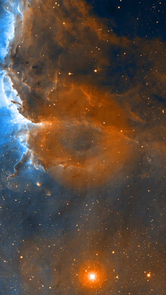 橙と茶のガスがうねる星雲の下に明るい一つ星が光っています。