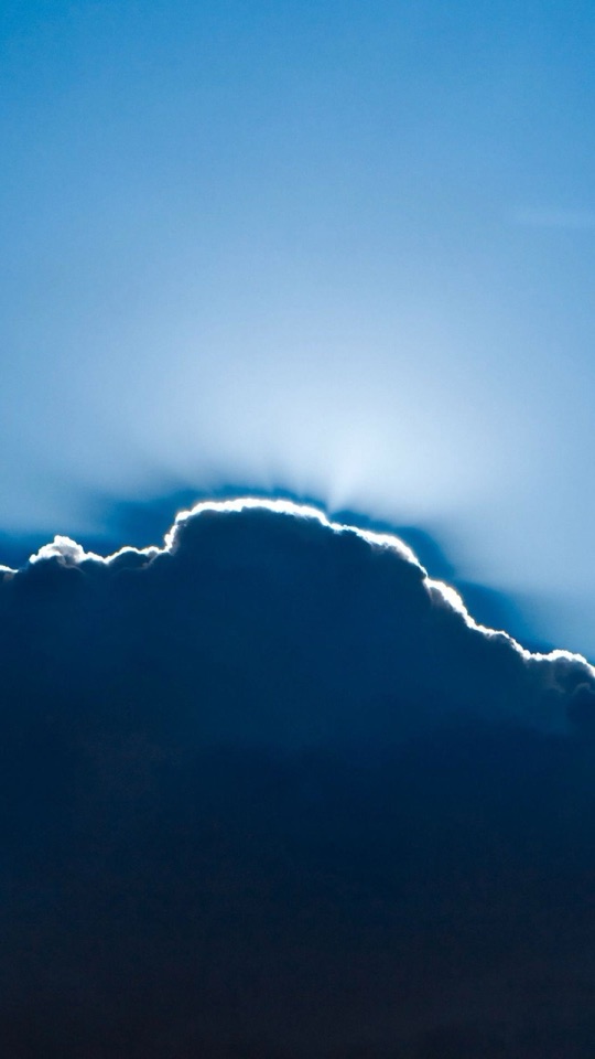 青空の中で、太陽を隠す雲の縁が白く光り輝く、ミニマルな空の写真。