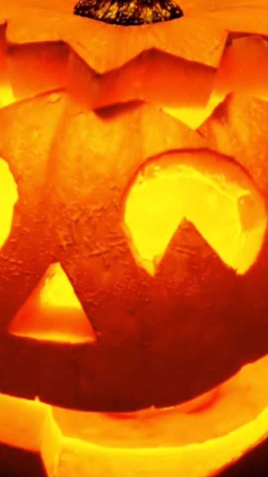 暗がりの中で、内側からオレンジ色に灯る、顔をくり抜いたハロウィンのかぼちゃの写真。