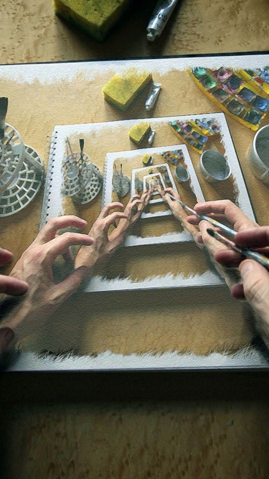 机の上で、道具を使って紙に螺旋状の作品を制作する手元をとらえた俯瞰写真。