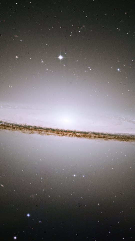 ハッブル宇宙望遠鏡の画像。黒い宇宙に、暗い塵の帯で縁取られた白い円盤状の銀河が横たわる。