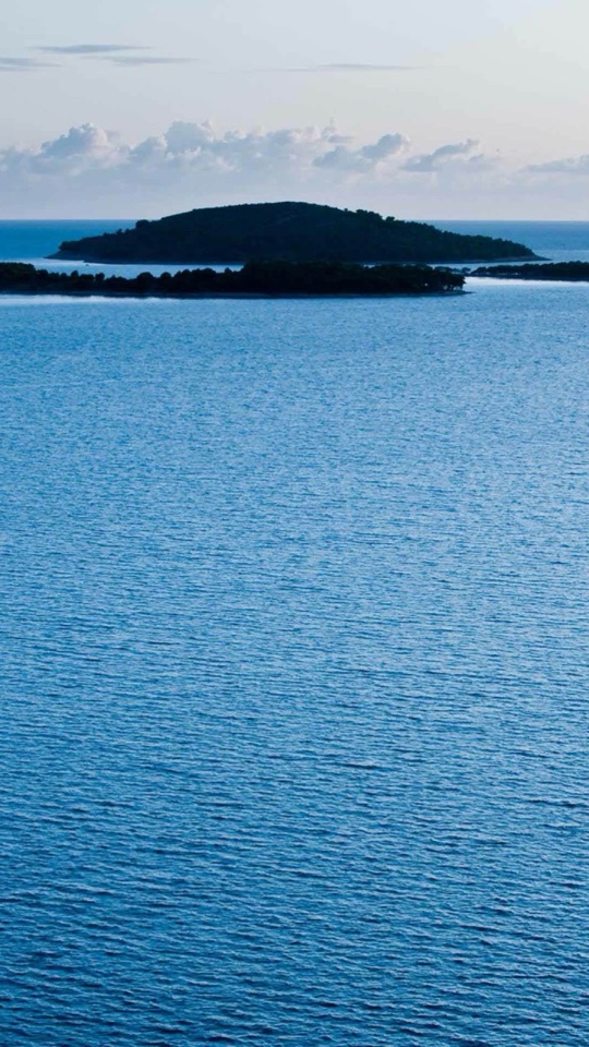 穏やかな青い海の中に、緑に覆われた小さな島がぽつんと浮かぶミニマルな写真。