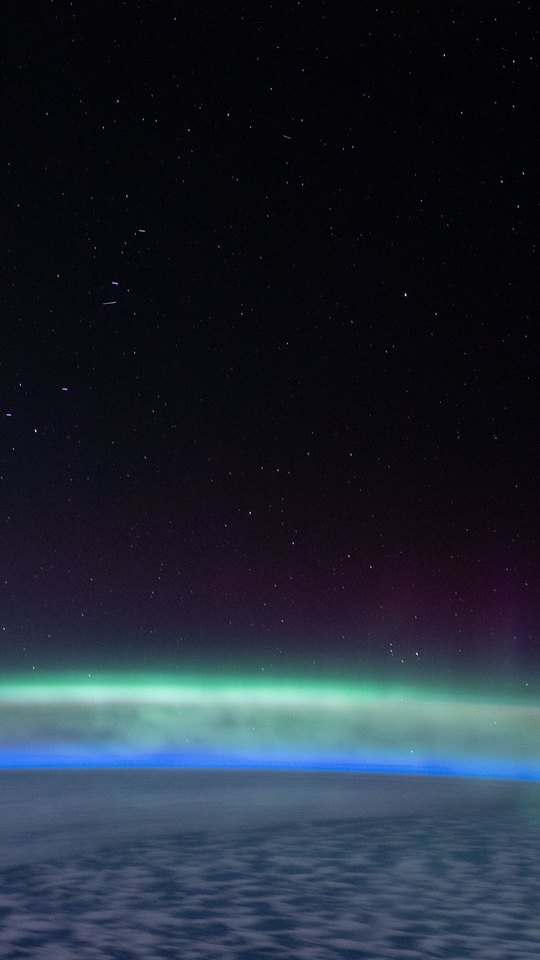 国際宇宙ステーションから撮影した写真。地球の縁に緑のオーロラが帯状に光り、上は星の見える黒い宇宙。