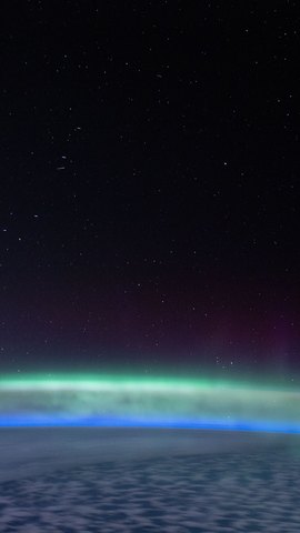 国際宇宙ステーションから撮影した写真。地球の縁に緑のオーロラが帯状に光り、上は星の見える黒い宇宙。