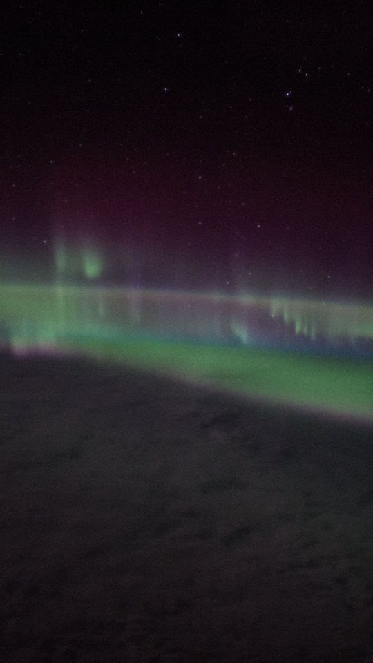 国際宇宙ステーションから撮影した写真。黒い宇宙と星の下、地球の縁に沿って緑のオーロラが光る。