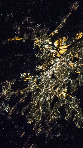 国際宇宙ステーションから見た夜の都市。黒い大地に、白と黄色の街明かりが密集する。