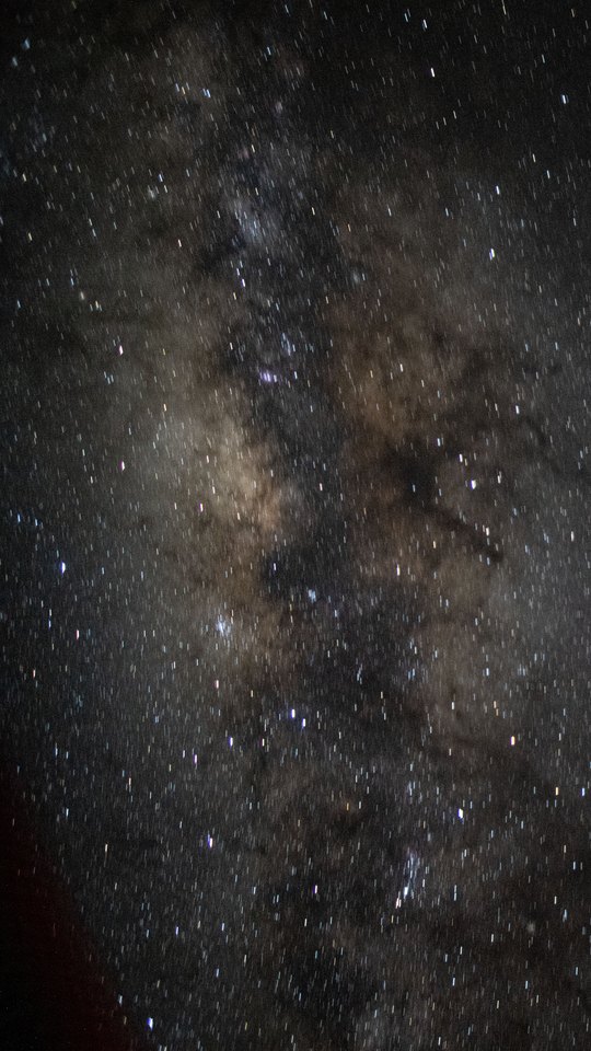 国際宇宙ステーションから撮った天の川。無数の星と暗い塵の帯が画面を埋め、左下に宇宙船の暗い影がかすかに写る。