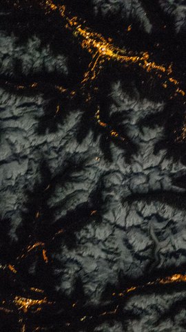 国際宇宙ステーションから見た夜の山岳地帯。月明かりに白く浮かぶ雪の尾根と、谷筋に点々と並ぶオレンジ色の町明かり。