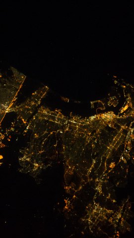 国際宇宙ステーションから見た夜の海岸都市。黒い海に沿って、オレンジ色の街明かりが広がる。