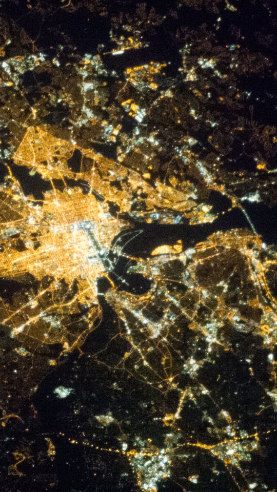 国際宇宙ステーションから見た夜のワシントンD.C.。オレンジ色の街明かりの格子を、黒い川が蛇行して横切る。