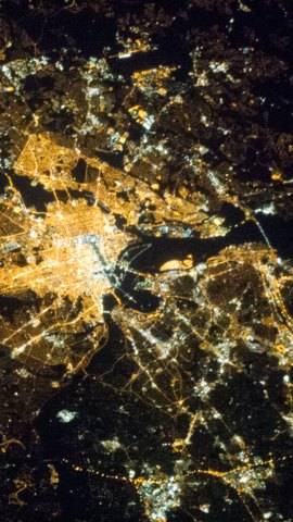国際宇宙ステーションから見た夜のワシントンD.C.。オレンジ色の街明かりの格子を、黒い川が蛇行して横切る。