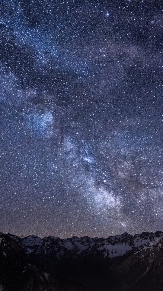山の稜線の上に、天の川が淡く立ちのぼる縦長の星空写真です。