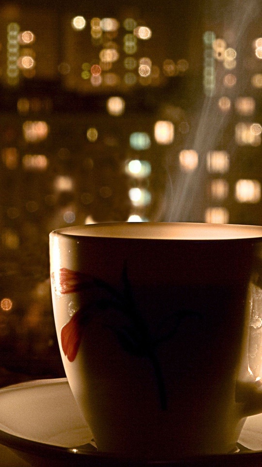 夜景のボケを背に、湯気の立つコーヒーカップが置かれています。