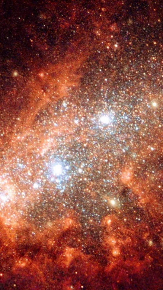 橙色に染まる銀河の中に、青白く輝く星団と無数の星がびっしりと散らばります。