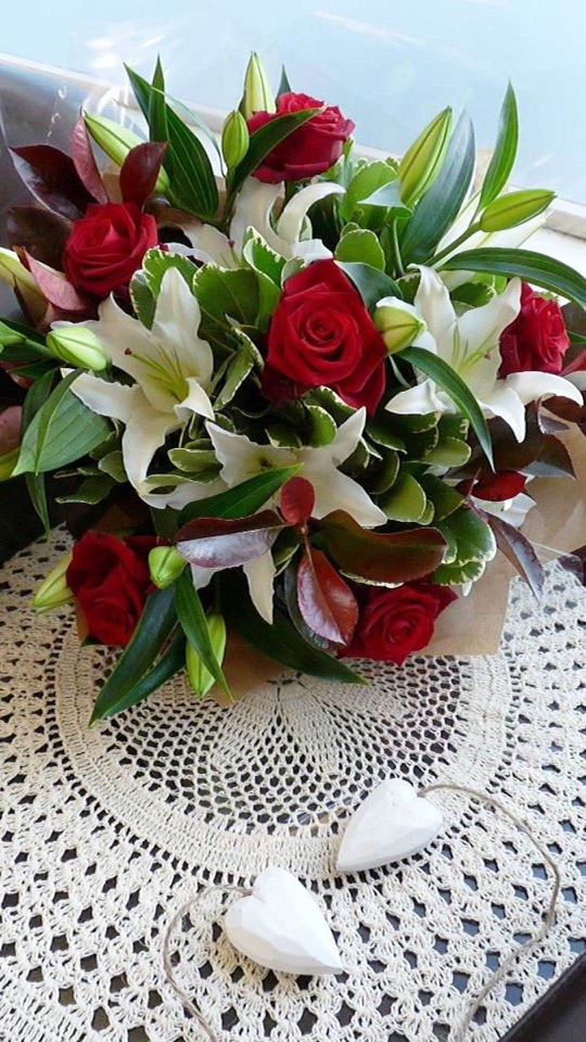 レース編みの上に赤い薔薇と白い百合の花束と木の心形が置かれる。
