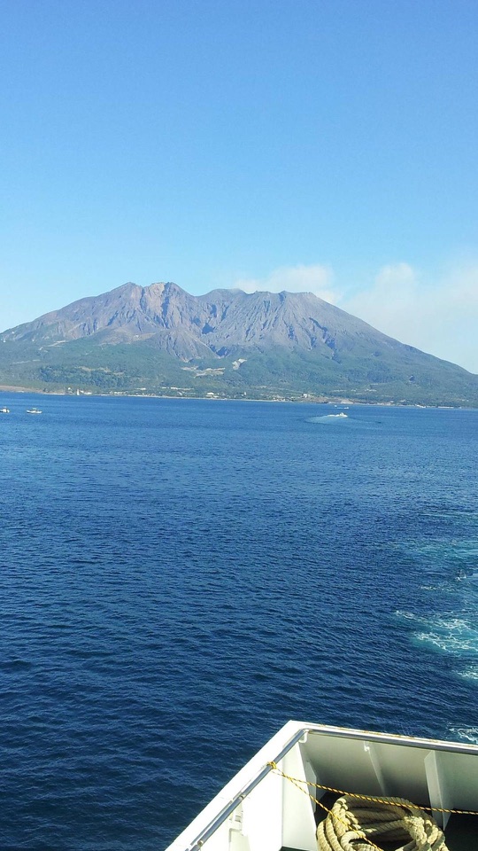 青い海の向こうになだらかな火山がそびえ手前に船の縁とロープが写ります。