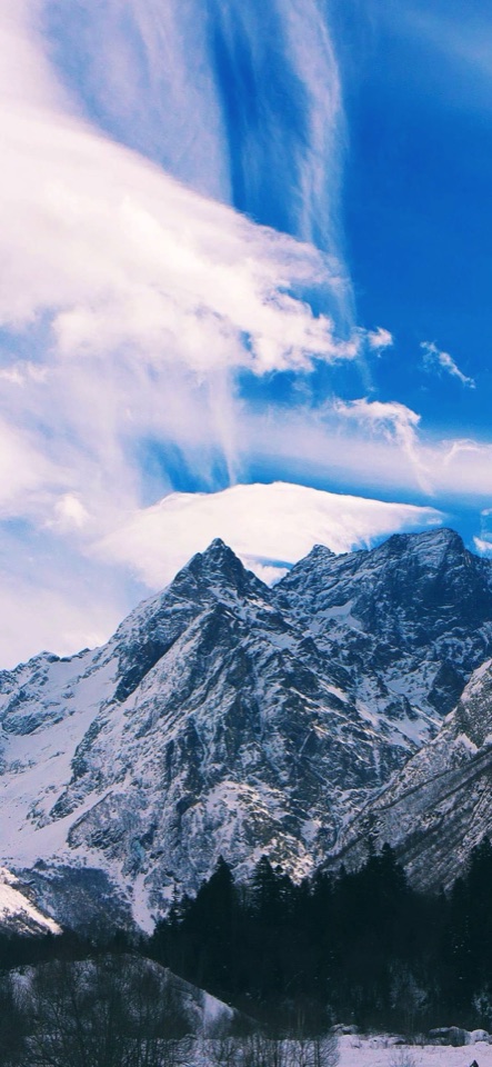 青空にたなびく雲の下、雪を頂いた鋭い山嶺がそびえる風景写真。