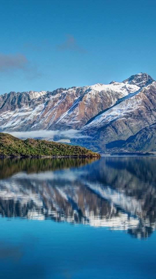 雪をいただく山並みが、鏡のように静かな湖面に対称に映り込む風景写真。