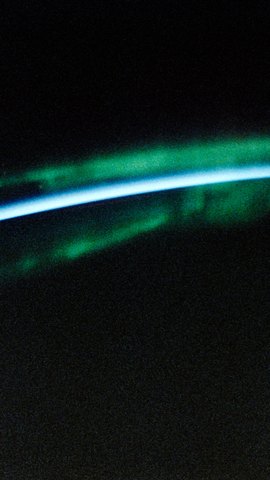 スペースシャトルから見た地球の縁。青く細い大気の線を、緑のオーロラが包んでいる。