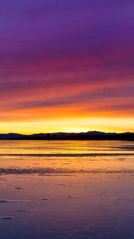 紫とオレンジに染まる夕焼けの空の下、凍った湖面が広がる静かな風景写真。