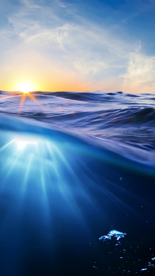 水平線に沈む夕日の上と、光が差し込む海中を同時にとらえた青い海の写真。
