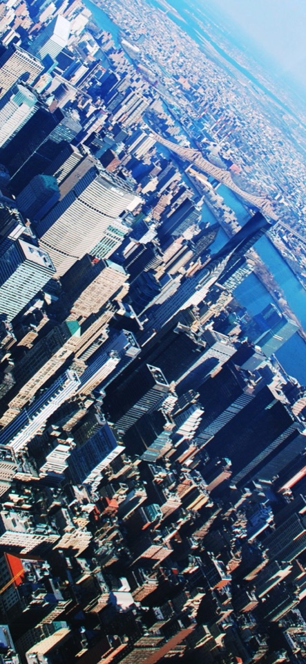青空を背に、高層ビルの密集する都市を斜めの角度で空撮した写真。